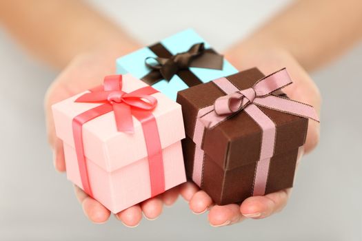 Cropped view image of a woman holding three colourful Christmas gifts with decorative ribbons and bows in the palms of her her hands, can also be used for anniversary, birthday or other celebration