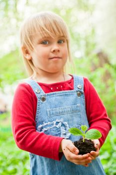 Blonde girl wearing red dress showing seeding with ground, focus on sprout