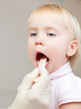 Pediatrician examining little girl's throat with tongue depressor