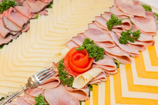 Party tray of assorted meats and cheeses with  flower made of tomato in the middle.