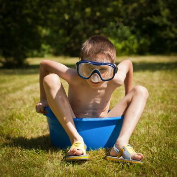 Boy wearing swimming mask sitting in a washbowl on a hot summer day
