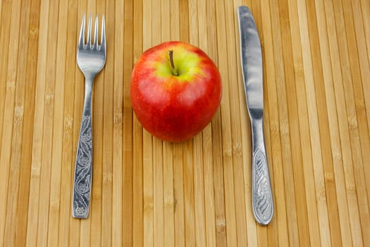 red apple lying on a bamboo napkin with cutlery