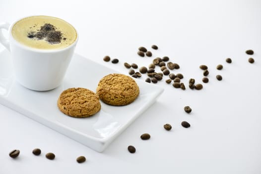 coffee beans next to a cup of coffee and biscuits on a plate