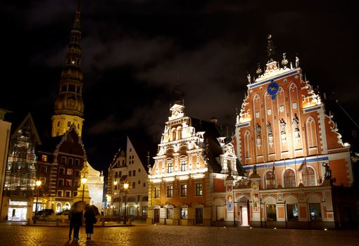 Beautiful old architecture of the central square of Riga. Night view with illuminated buildings and people silhouettes.