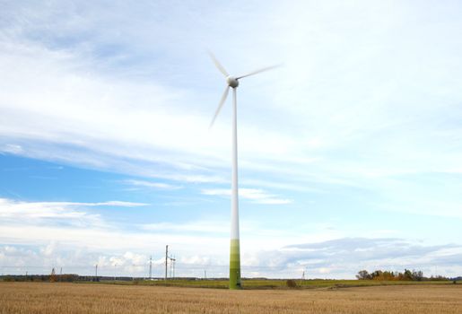 Wind turbine with motion blurred blades over the blue sky with clouds.