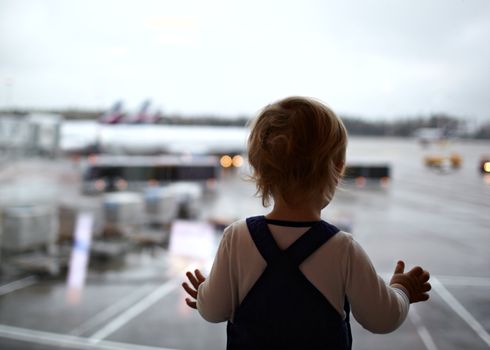 Two year old babyboy is looking at the planes in the airport.
