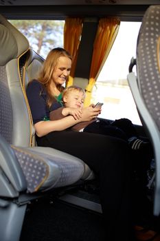 Young mother is playing games on the phone with her son, while travelling by bus.