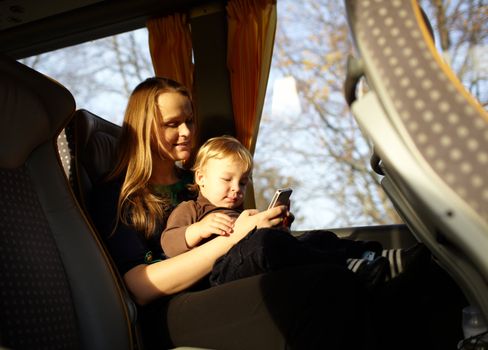 Young mother is playing games on the phone with her son, while travelling by bus. Beautiful natural light.
