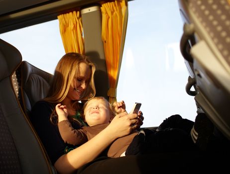 Young mother is playing games on the phone with her son, while travelling by bus. Boy is smiling and screwing up his eyes.