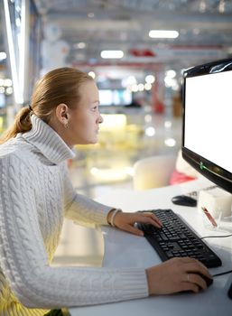 Young girl is working at the computer in the business center. The monitor screen is white.