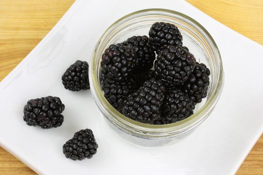 Blackberries in a jar, on a white plate sitting on a wooden counter top.