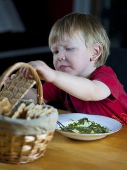 Young caucasian boy eating spinach soup and crispbread