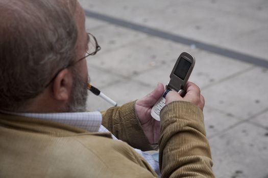 SENIOR MAN WITH MOBILE, OVIEDO, SPAIN - SEPTEMBER 17: Caucasian male with mobile phone is texting a message on a bench in city of Oviedo, Spain, on September 17, 2012.