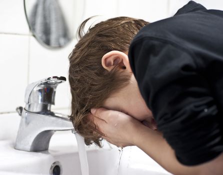 Young boy in domestic bathroom washing his face with water