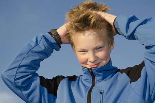 Kid adjusts his spiky hairstyle against blue sky background