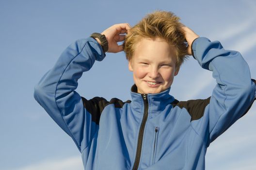 Teenager adjusts his hair against blue sky background