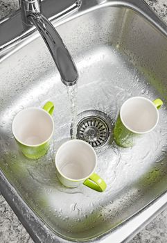 Washing green cups in the kitchen sink. Water running from the tap.