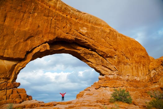 Woman staying with raised hands inside an Arch in the Arches National Park, UT