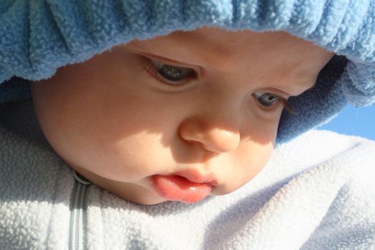 A close up of a baby in a blue fleece jacket with the hood up