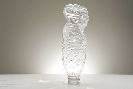 Empty recyclable plastic water bottle covered in water droplets and already partially twisted and compressed for recycling standing on its neck on a studio countertop