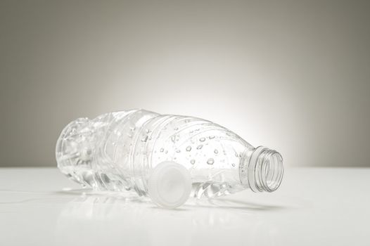 Clear empty plastic bottle with water droplets lying on its side on a white countertop alongside the cap after consumption of a pure refreshing drink