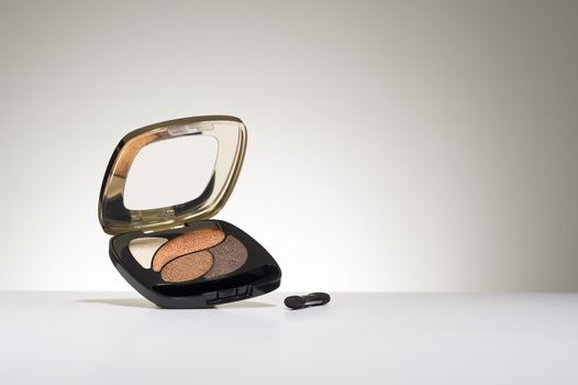 Opened cosmetics compact with three shades of trendy eyeshadow suspended in the air on a white studio background with a small applicator brush in the foreground