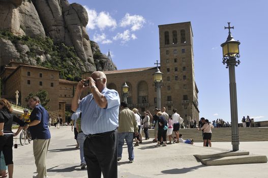 Barcelona, Spain - June 20, 2010 :  man takes photo among walking tourists at the place of famous Monserrat Monastery at Barcelona's vicinity.