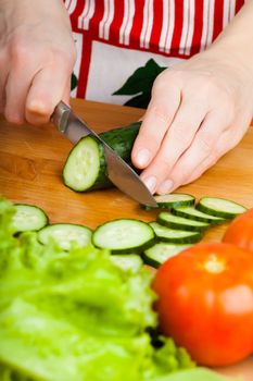 Woman cutting vegetables (tomato, cucumber, salad) on a wooden table