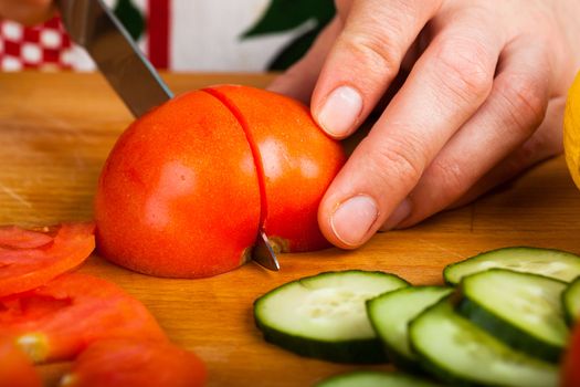 Woman cutting vegetables (tomato, cucumber, salad) on a wooden table