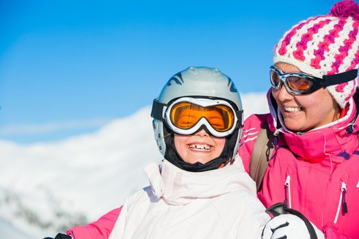 Portrait of happy smiling girl in ski goggles and with her mother, Zellertal, Austria. Focus on the girl