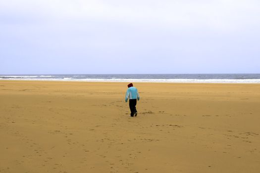 a lone girl walking against the cold wind on Ballybunion beach