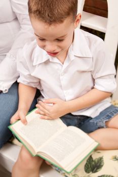 Cute Young Boy Reading His Book Indoors Next to His Mom.