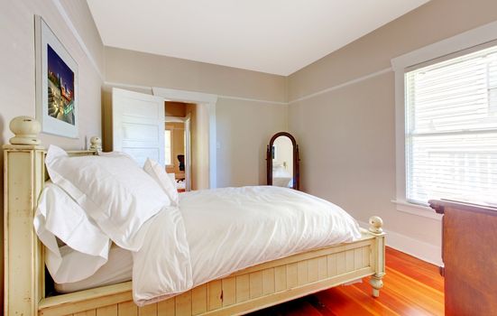 Bright bedroom with white bed, beige walls and hardwood floor.