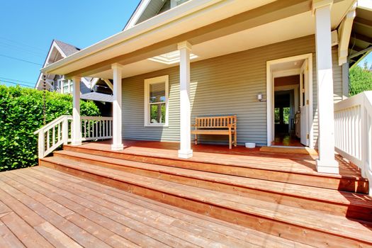 Back porch of small grey house with bench dring sunny summer day.