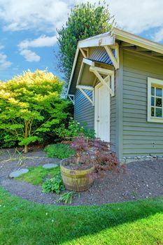 Grey small outdoor shed with backyard landscape with green summer grass.