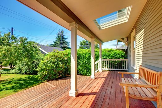 Large covered porch with skylight and wood bench and floor with summer landscape.