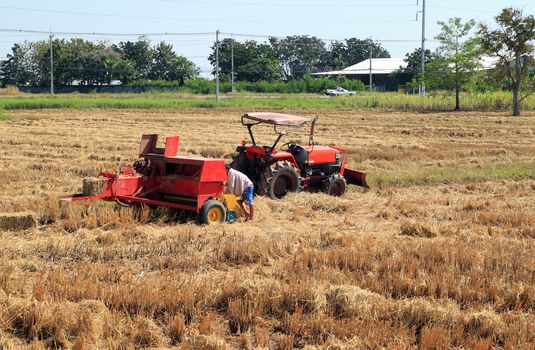 farmer and tractor packing straw in the field at Thailand