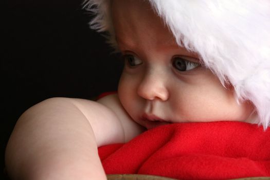 A close-up of a baby in a santa hat, looking pensive.