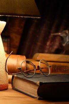 Vintage still life with old spectacles on book near desk lamp