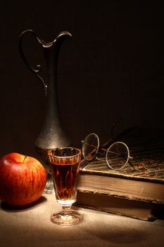 Vintage still life with apple and drink near old book on canvas surface