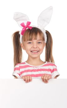 Easter concept image. Portrait of happy little girl with bunny ears and empty white board over white background.