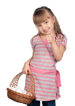 Happy little girl holding basket of eggs and giving you thumb up over white background