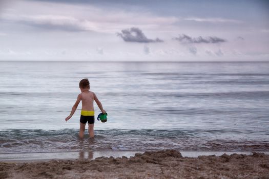 boy walks into cold sea water in a bucket to scoop up