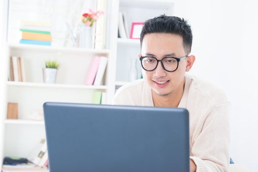 Southeast Asian male using notebook online at home, indoor living lifestyle