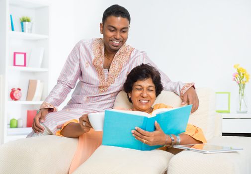 Mature 50s Indian woman reading a book with her son at home