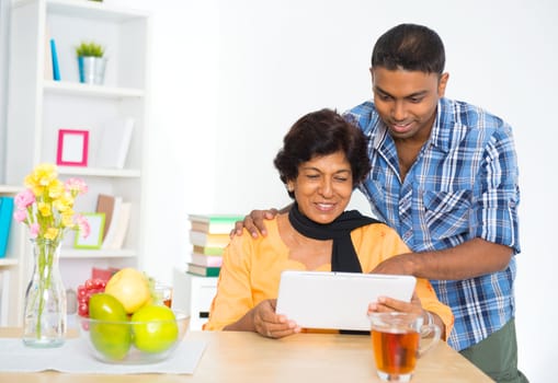 Mature 50s Indian woman and son using digital computer tablet at home