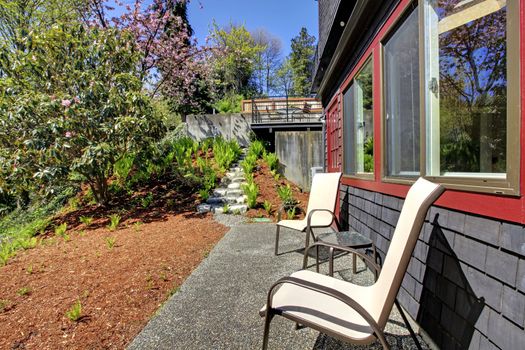 Spring Back yard with two chairs and black wood house with red.