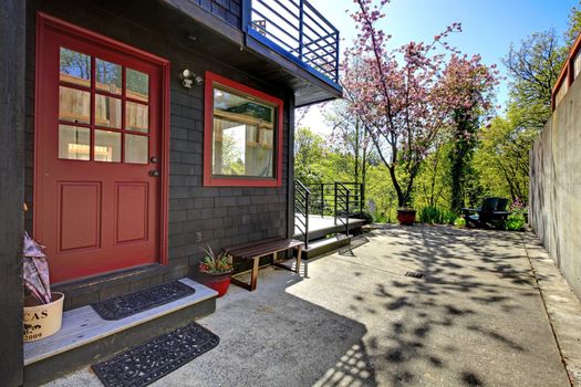Front red door of black wood house with garden view during spring.