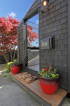 Black wood house with door and red flower pots with japaneas maple.