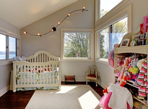 Baby girl room with white crib and clothes with many windows.